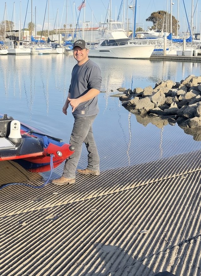 Tyler Calvet at a marina launch ramp beside the BOATIE unmanned surface vehicle